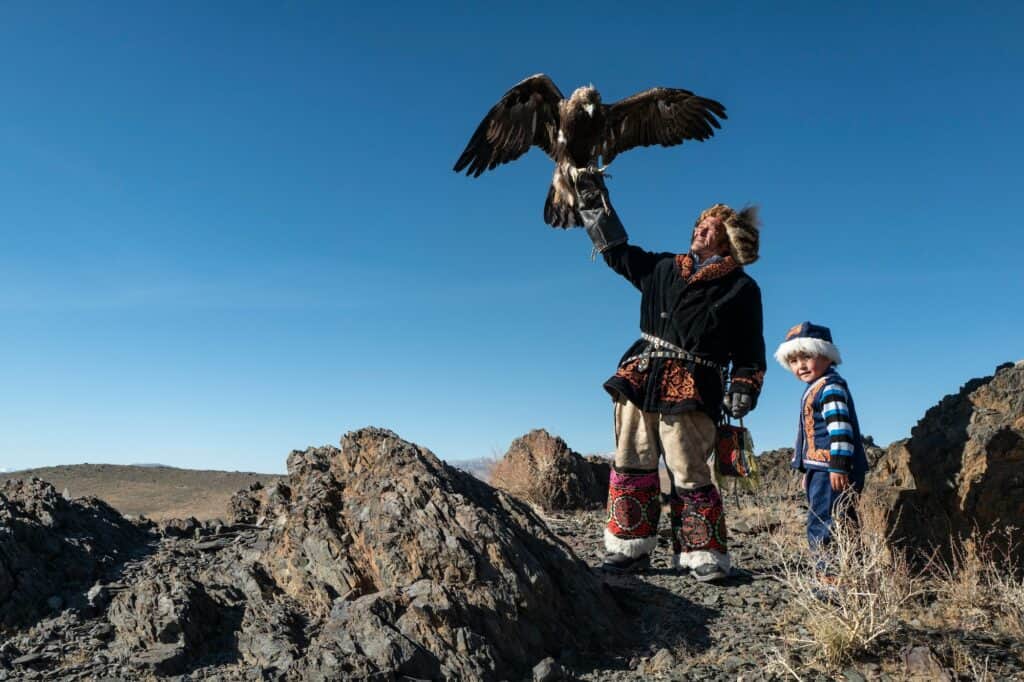 Mongolia Eagle hunter holding and eagle next to his son