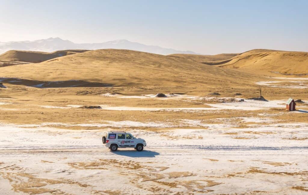 An offroad mongolia winter tour car drives near Elsen Taserkhai during winter, on the road to visit one of many winter events in Mongolia.