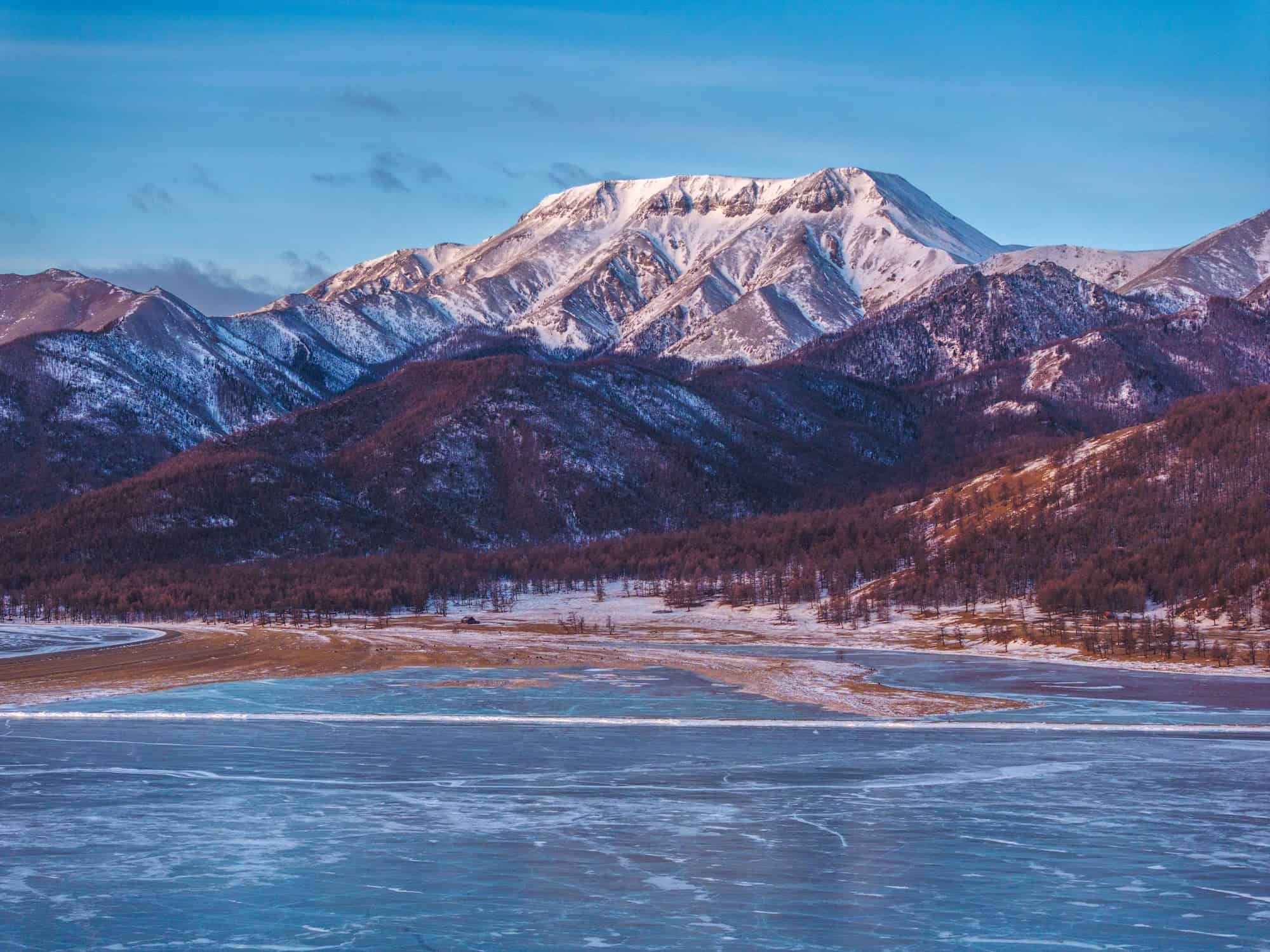 Ein zugefrorener See in der nördlichen Mongolei mit einem schneebedeckten Berg im Hintergrund